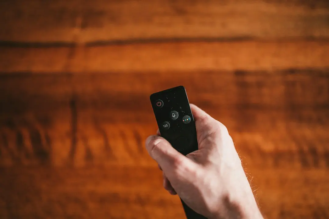 Una mano sostiene un mando a distancia negro sobre un fondo de madera
