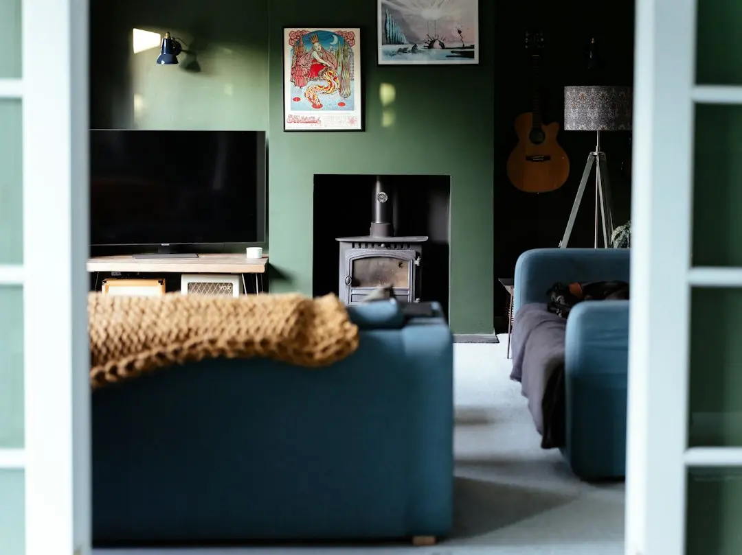 Un salón de paredes verdes con un televisor, un sofá azul y una estufa de leña